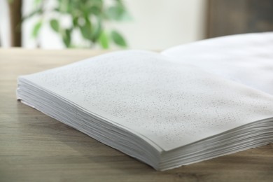 Photo of Book with Braille text on wooden table, closeup. Education and leisure for blind people