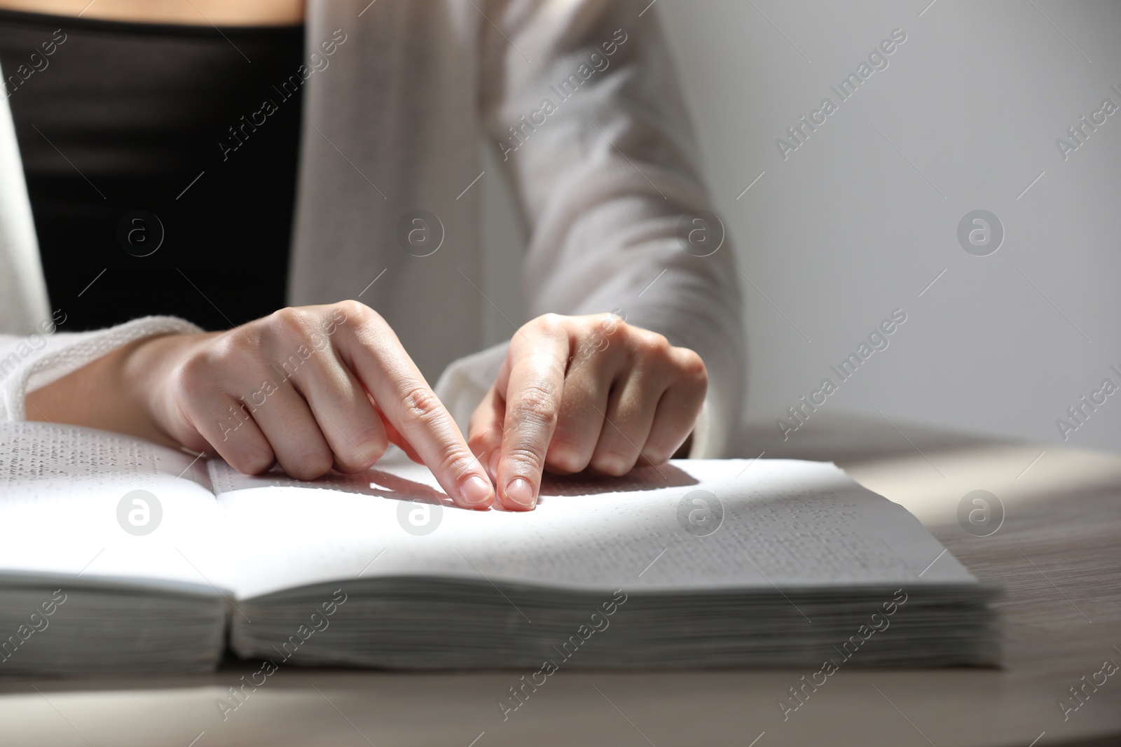 Photo of Blind woman reading book written in Braille at wooden table, closeup