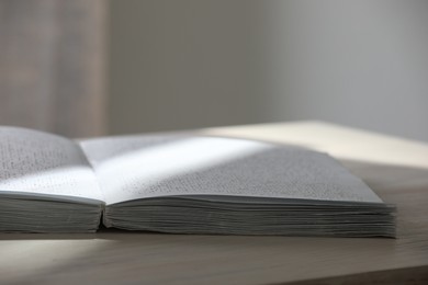 Photo of Book with Braille text on wooden table, closeup. Education and leisure for blind people