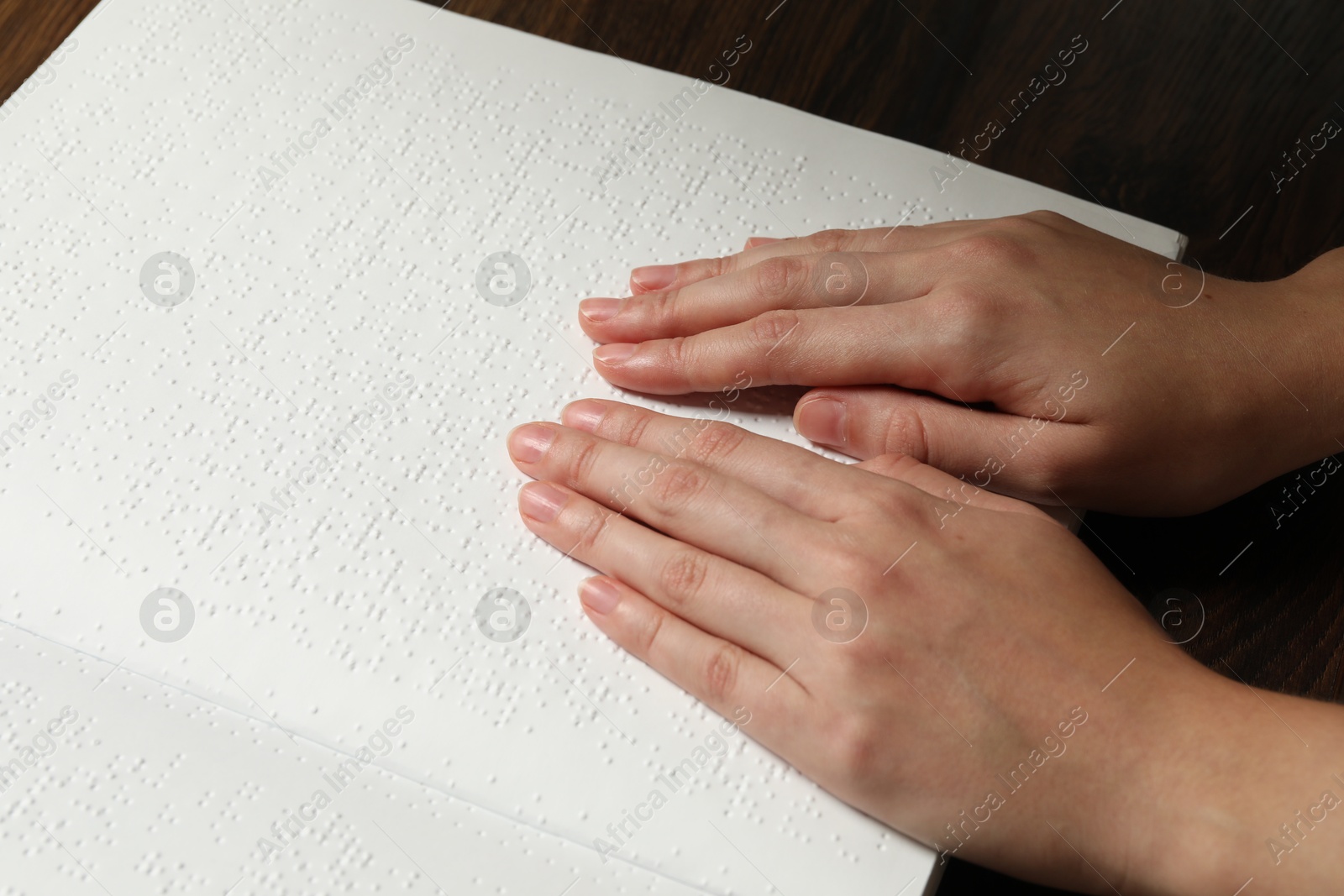 Photo of Blind woman reading book written in Braille at wooden table, closeup