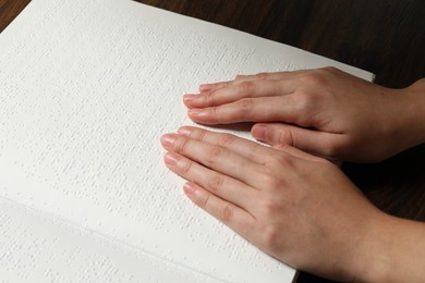 Photo of Blind woman reading book written in Braille at wooden table, closeup