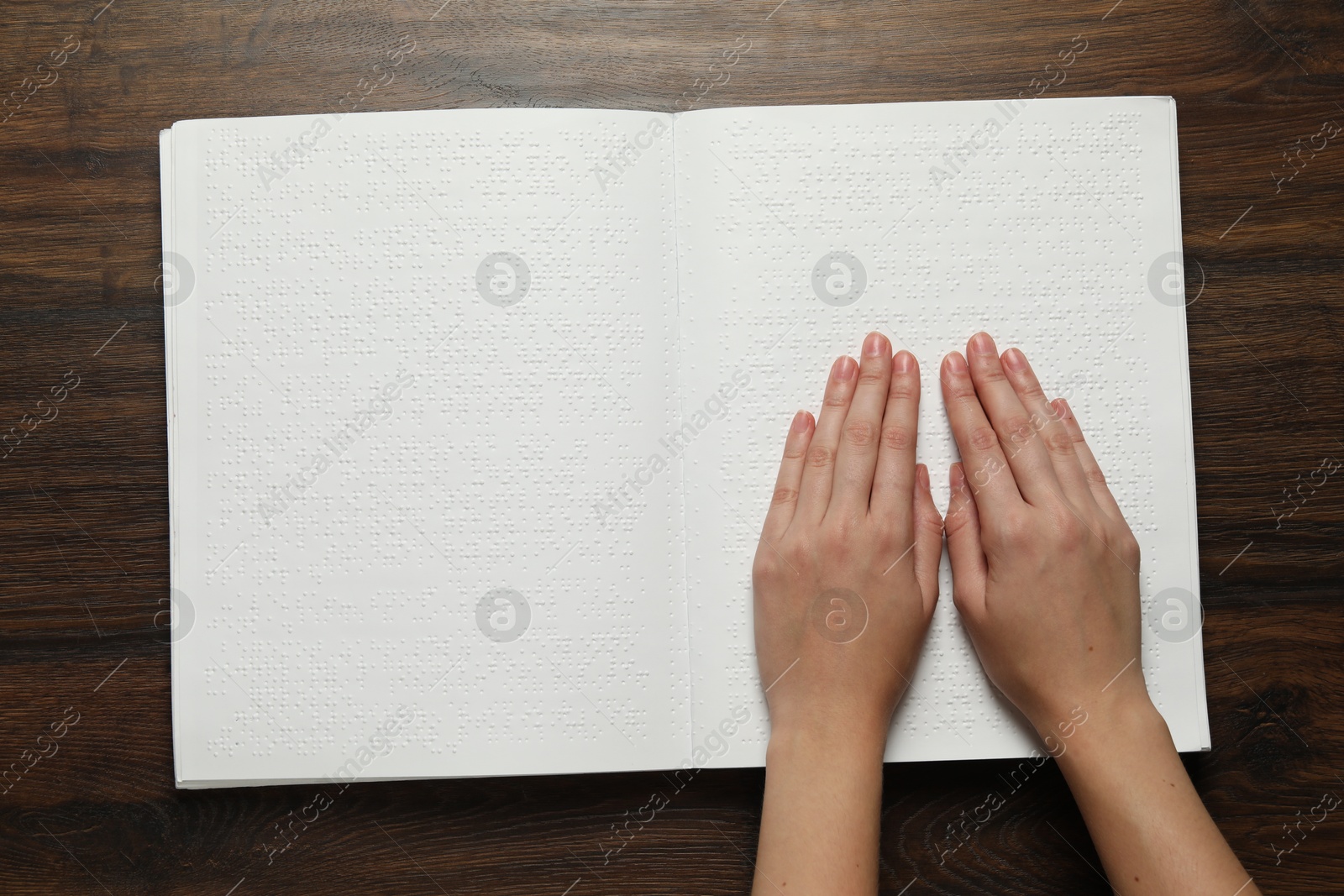 Photo of Blind woman reading book written in Braille at wooden table, top view