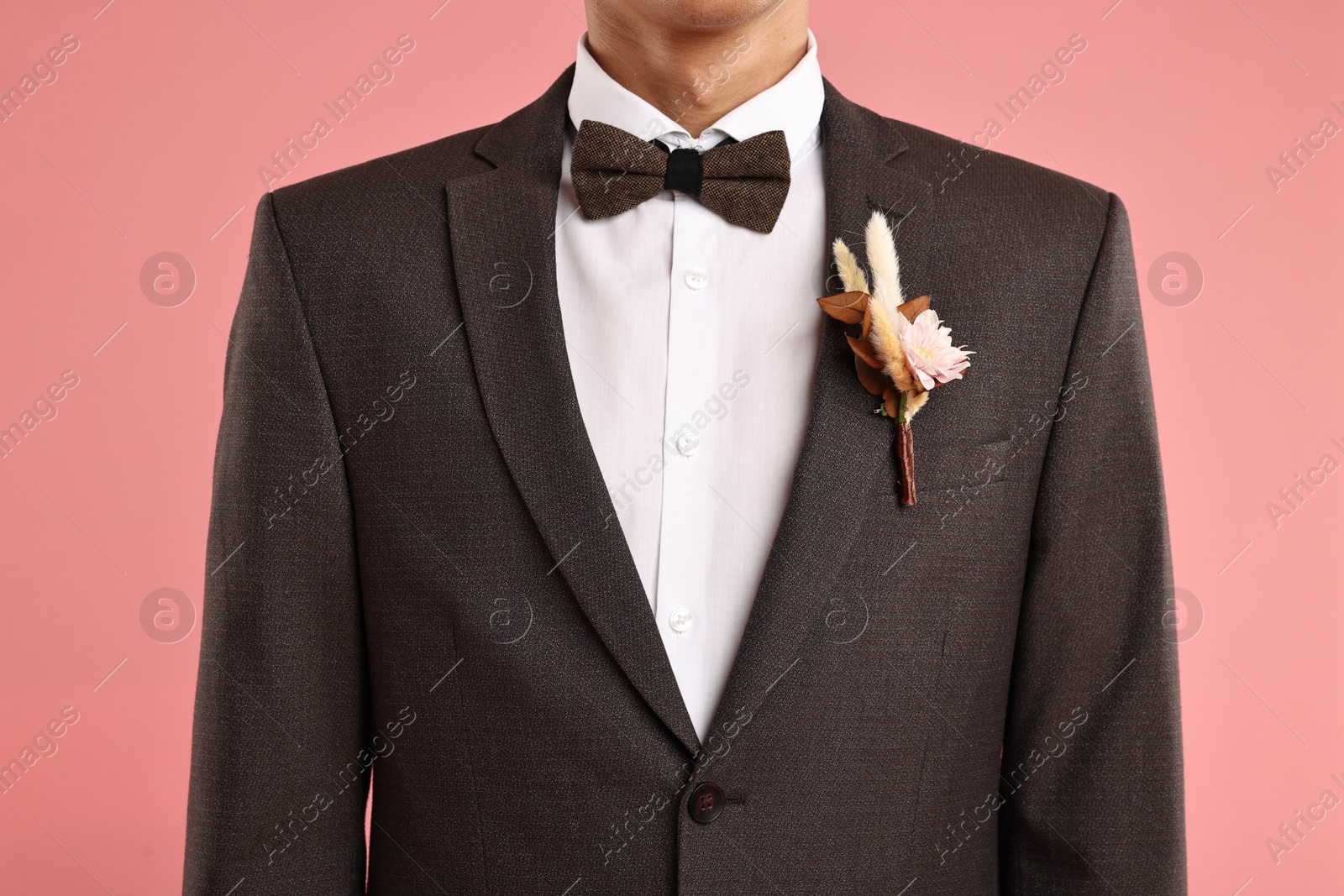 Photo of Groom in suit with stylish boutonniere on pink background, closeup