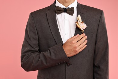 Photo of Groom in suit with stylish boutonniere on pink background, closeup