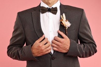 Photo of Groom in suit with stylish boutonniere on pink background, closeup