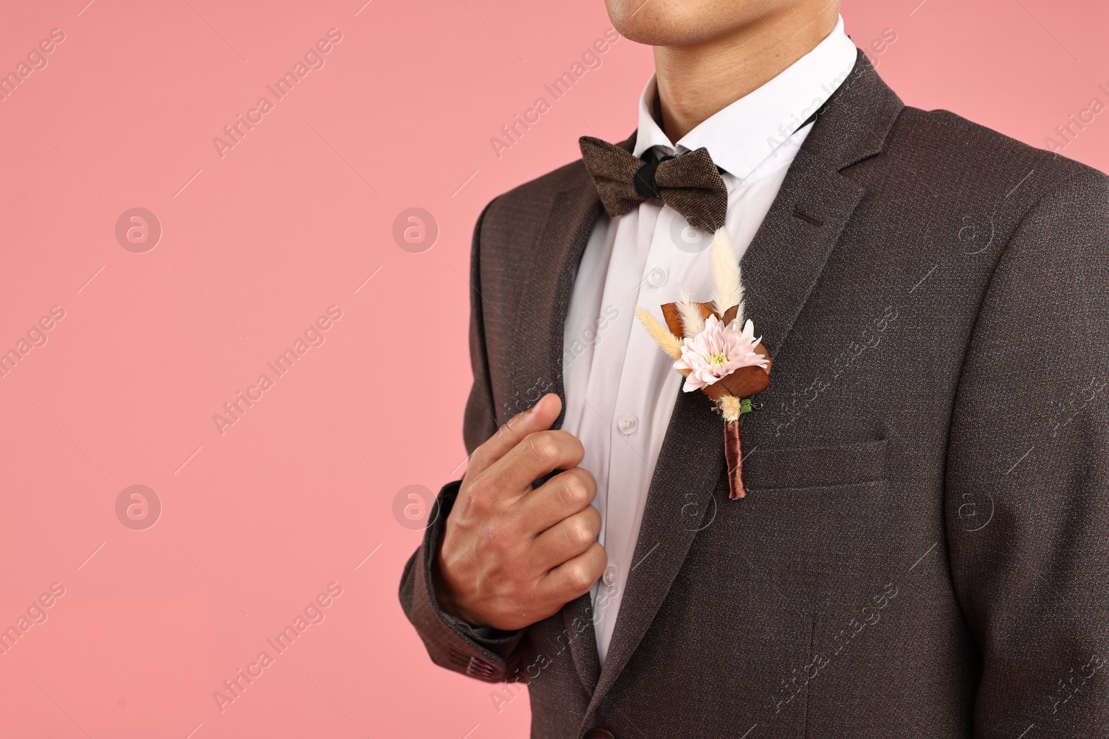 Photo of Groom in suit with stylish boutonniere on pink background, closeup. Space for text