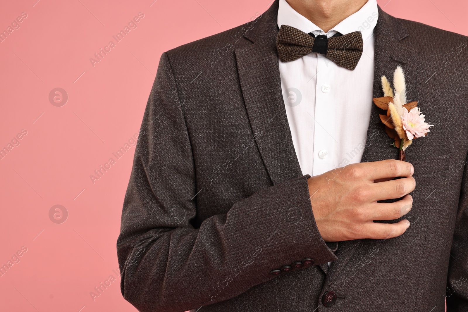 Photo of Groom in suit with stylish boutonniere on pink background, closeup