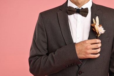 Groom in suit with stylish boutonniere on pink background, closeup