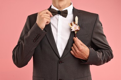 Photo of Groom in suit with stylish boutonniere on pink background, closeup