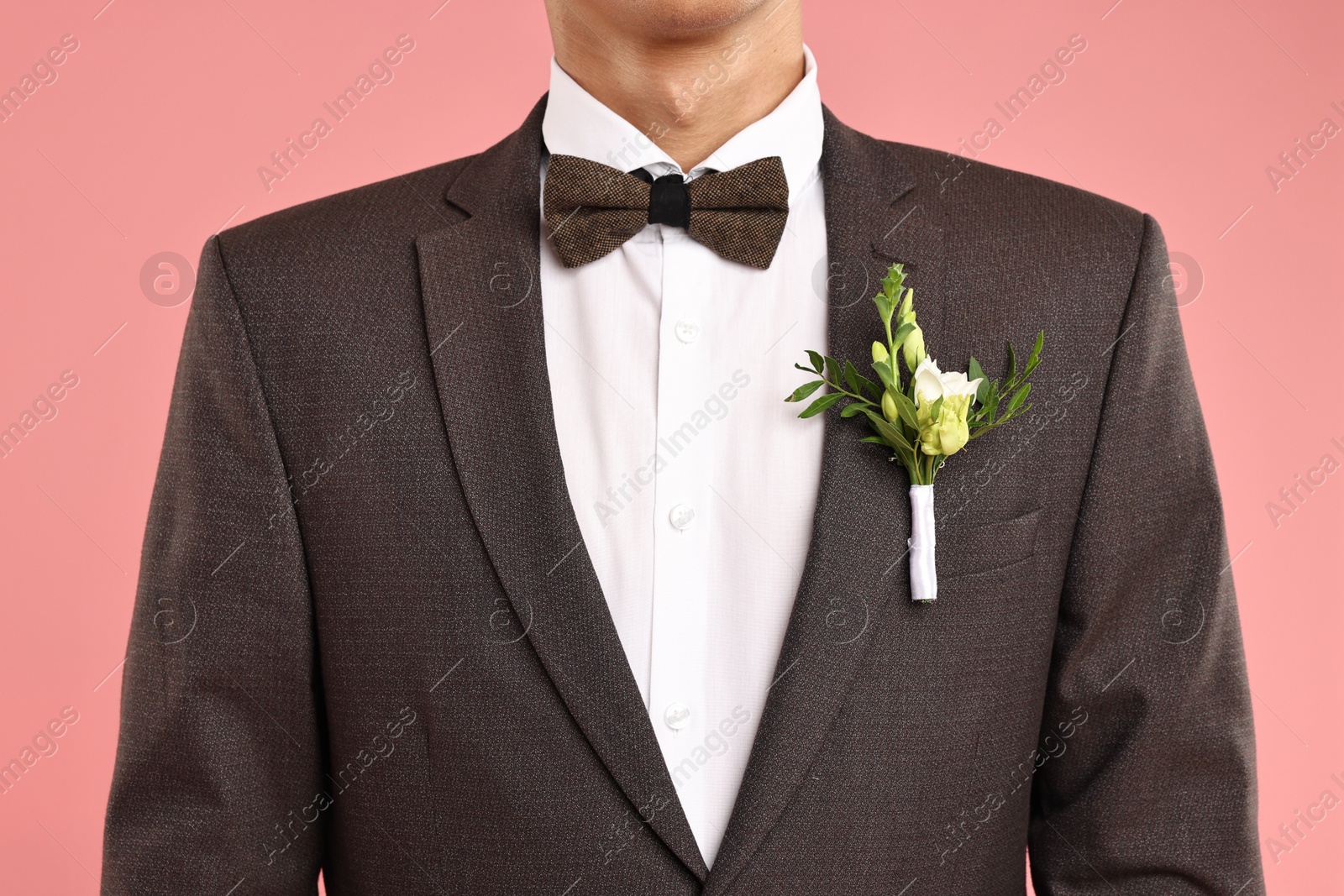 Photo of Groom in suit with stylish boutonniere on pink background, closeup