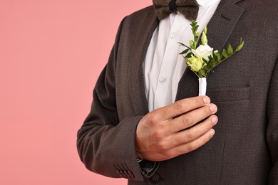 Photo of Groom in suit with stylish boutonniere on pink background, closeup