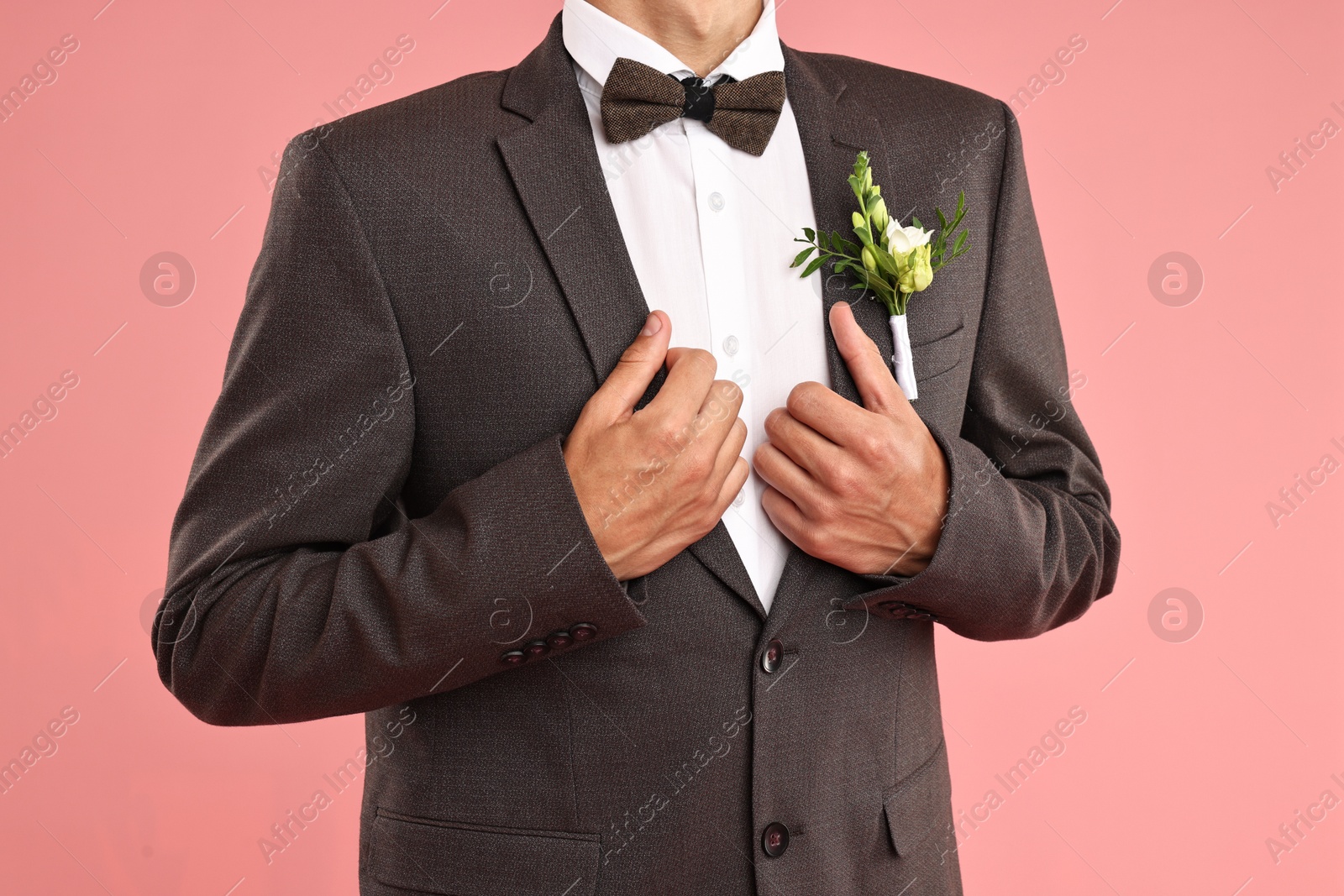 Photo of Groom in suit with stylish boutonniere on pink background, closeup