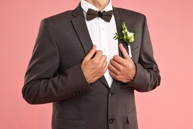 Photo of Groom in suit with stylish boutonniere on pink background, closeup