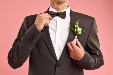 Photo of Groom in suit with stylish boutonniere on pink background, closeup