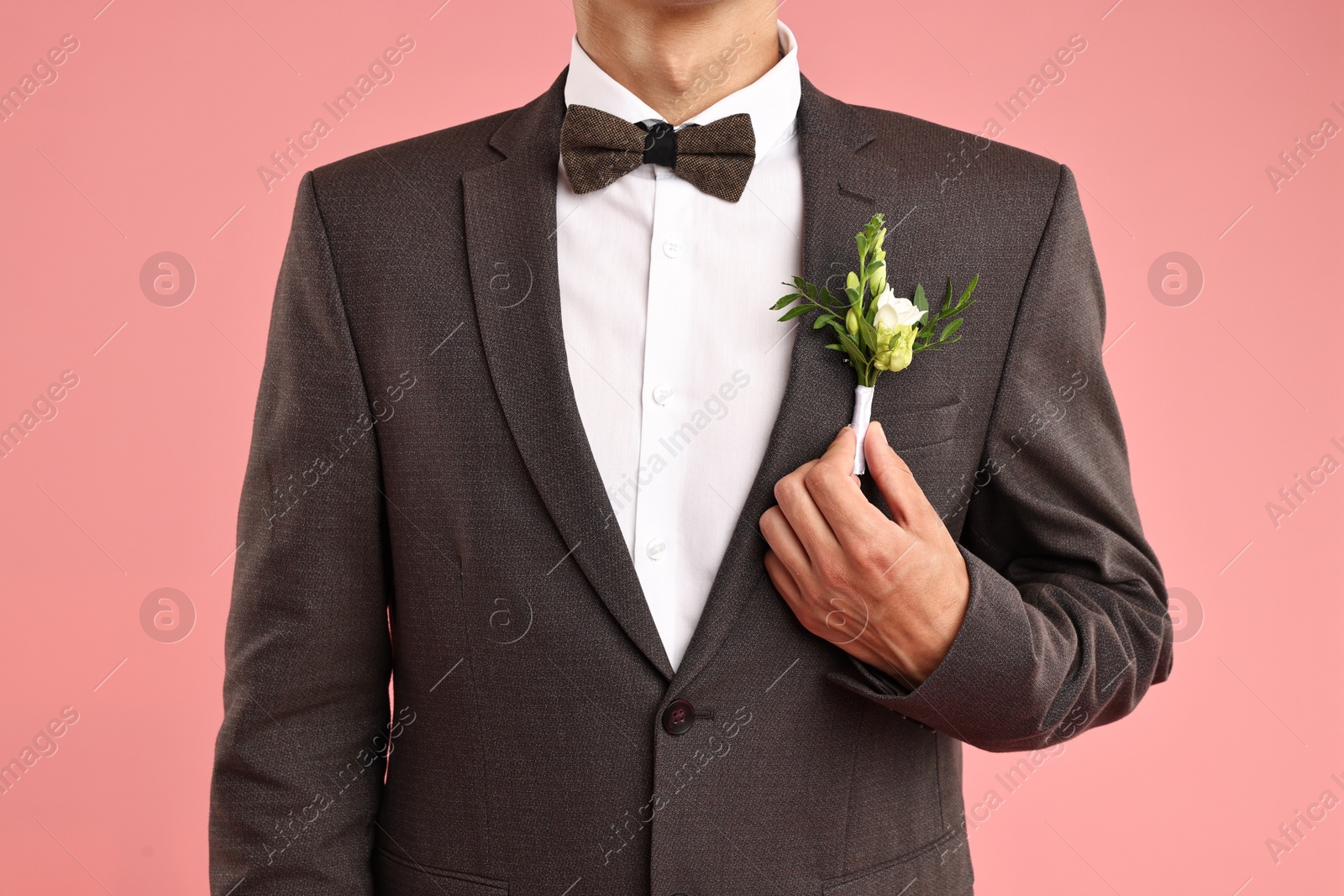 Photo of Groom in suit with stylish boutonniere on pink background, closeup