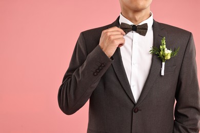 Photo of Groom in suit with stylish boutonniere on pink background, closeup. Space for text