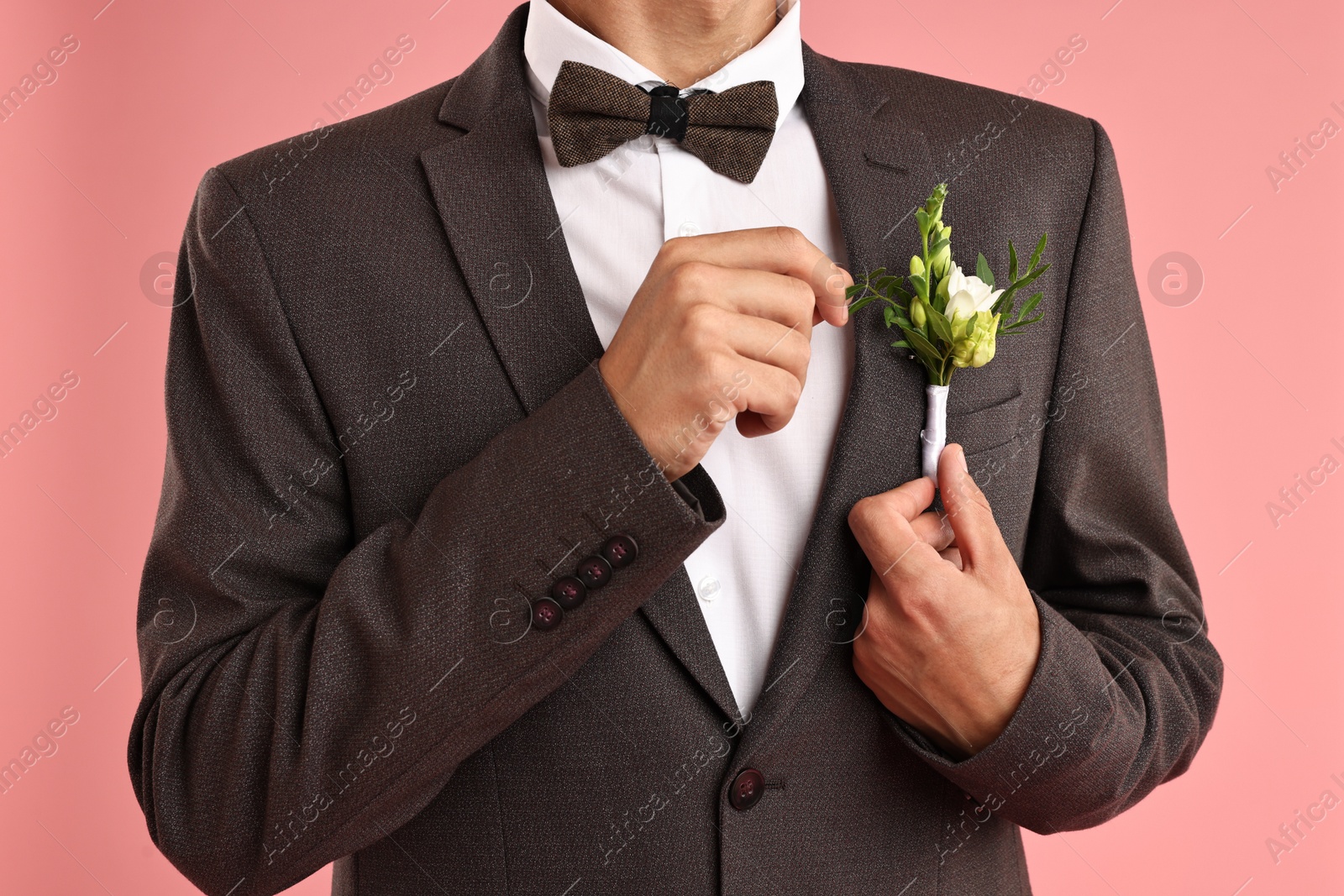 Photo of Groom in suit with stylish boutonniere on pink background, closeup