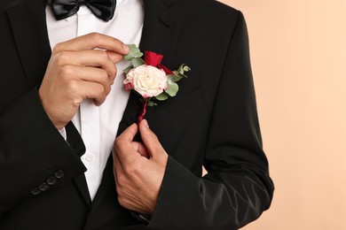 Photo of Groom in suit with stylish boutonniere on beige background, closeup