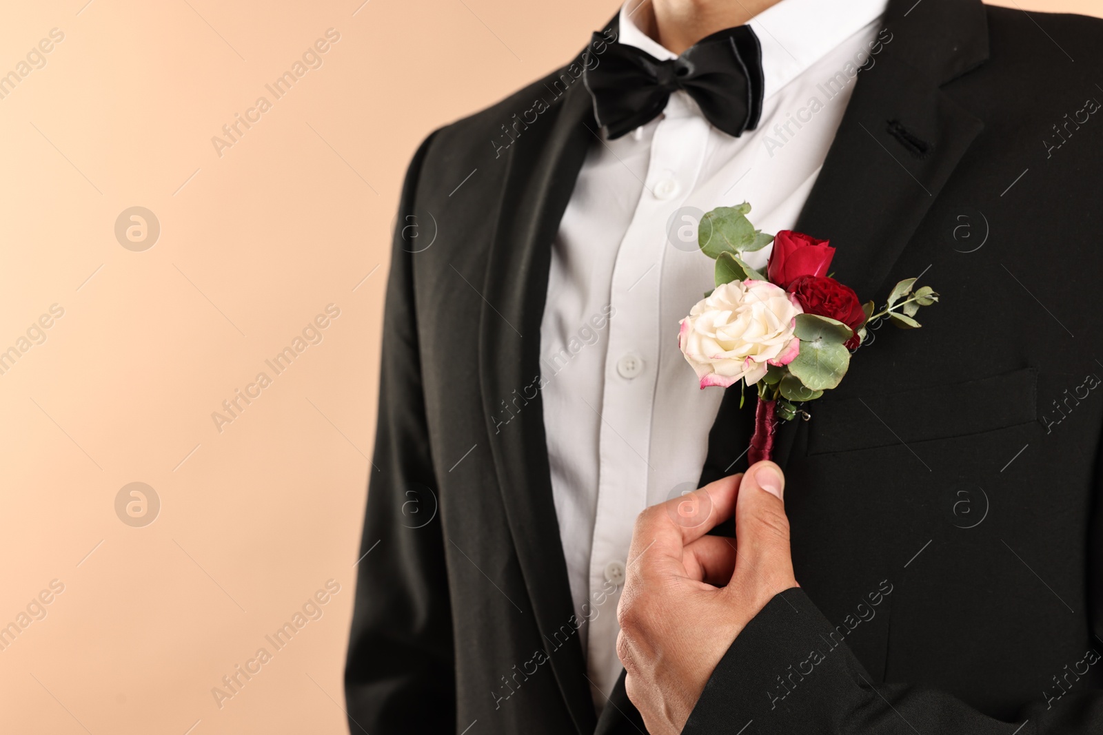 Photo of Groom in suit with stylish boutonniere on beige background, closeup. Space for text