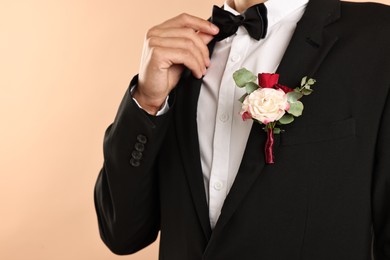 Photo of Groom in suit with stylish boutonniere on beige background, closeup