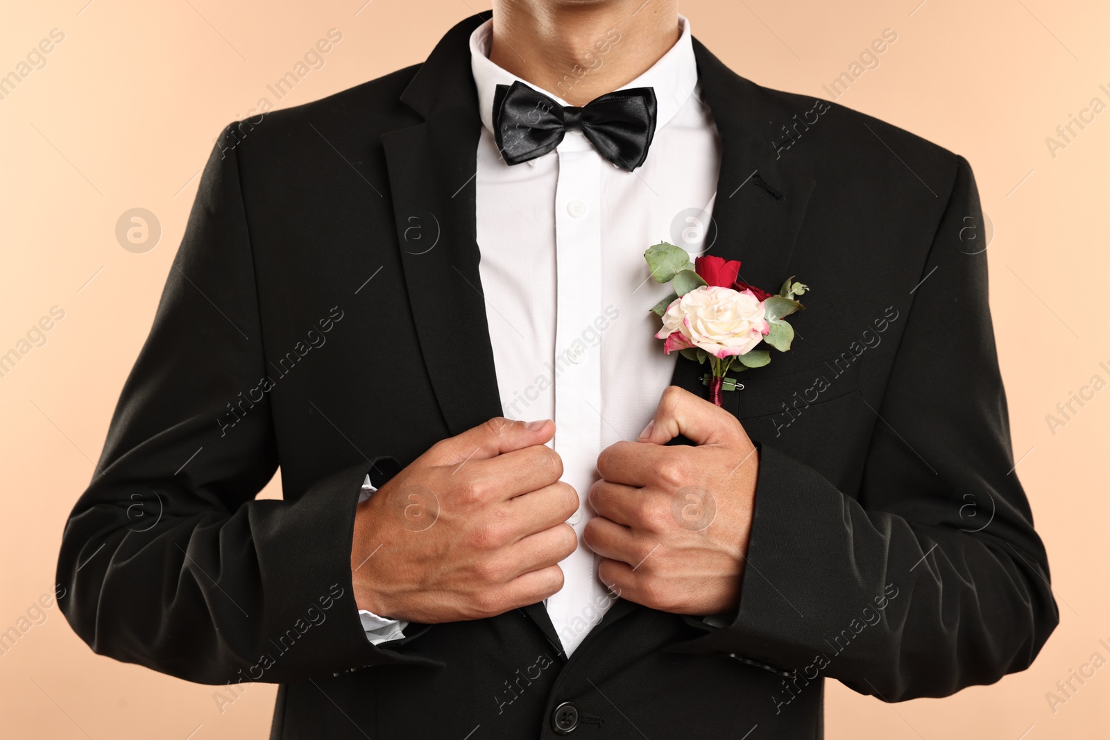 Photo of Groom in suit with stylish boutonniere on beige background, closeup