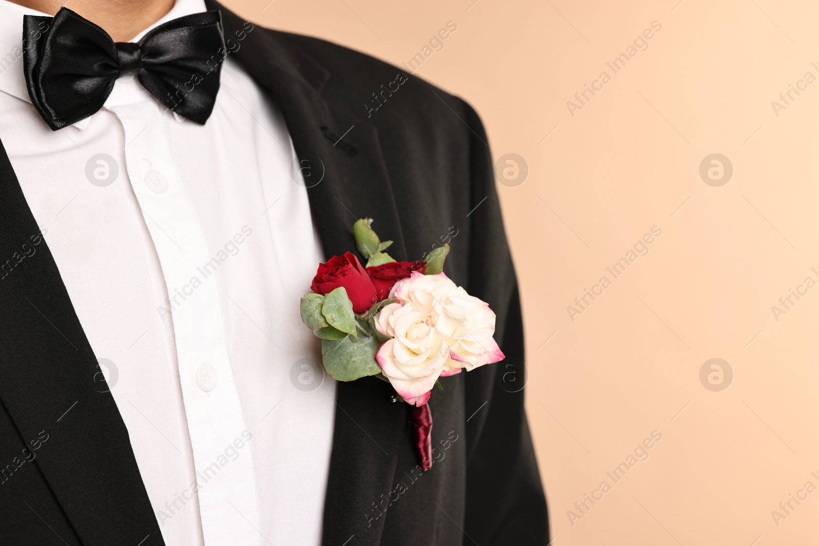 Photo of Groom in suit with stylish boutonniere on beige background, closeup. Space for text