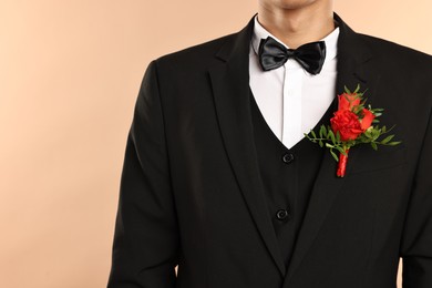 Photo of Groom in suit with stylish boutonniere on beige background, closeup