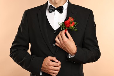 Photo of Groom in suit with stylish boutonniere on beige background, closeup