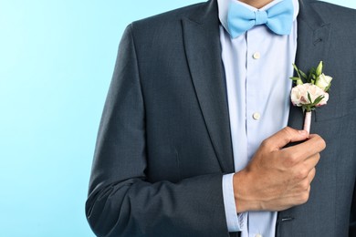 Photo of Groom in suit with stylish boutonniere on light blue background, closeup