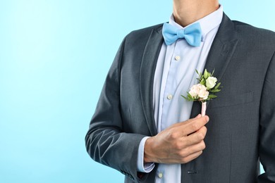 Photo of Groom in suit with stylish boutonniere on light blue background, closeup. Space for text