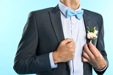 Photo of Groom in suit with stylish boutonniere on light blue background, closeup