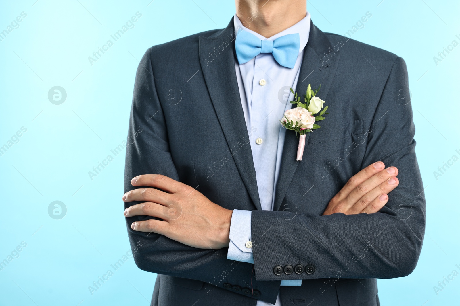 Photo of Groom in suit with stylish boutonniere on light blue background, closeup