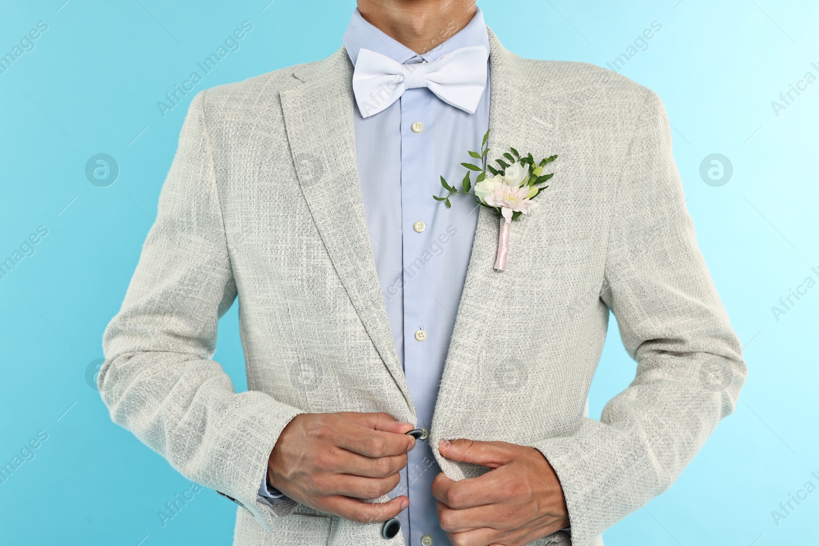 Photo of Groom in suit with stylish boutonniere on light blue background, closeup