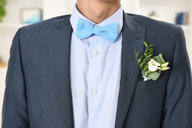 Groom in suit with stylish boutonniere indoors, closeup