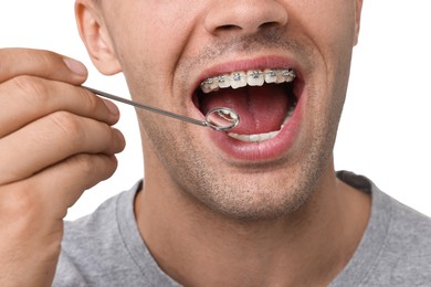 Photo of Examination of man's teeth with braces using mirror tool on white background, closeup