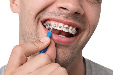 Man with dental braces cleaning teeth using interdental brush on white background, closeup