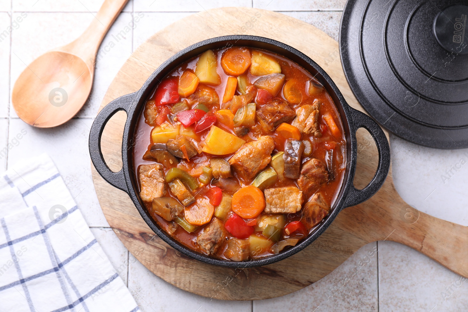 Photo of Delicious stew with vegetables in pot and spoon on light textured table, flat lay