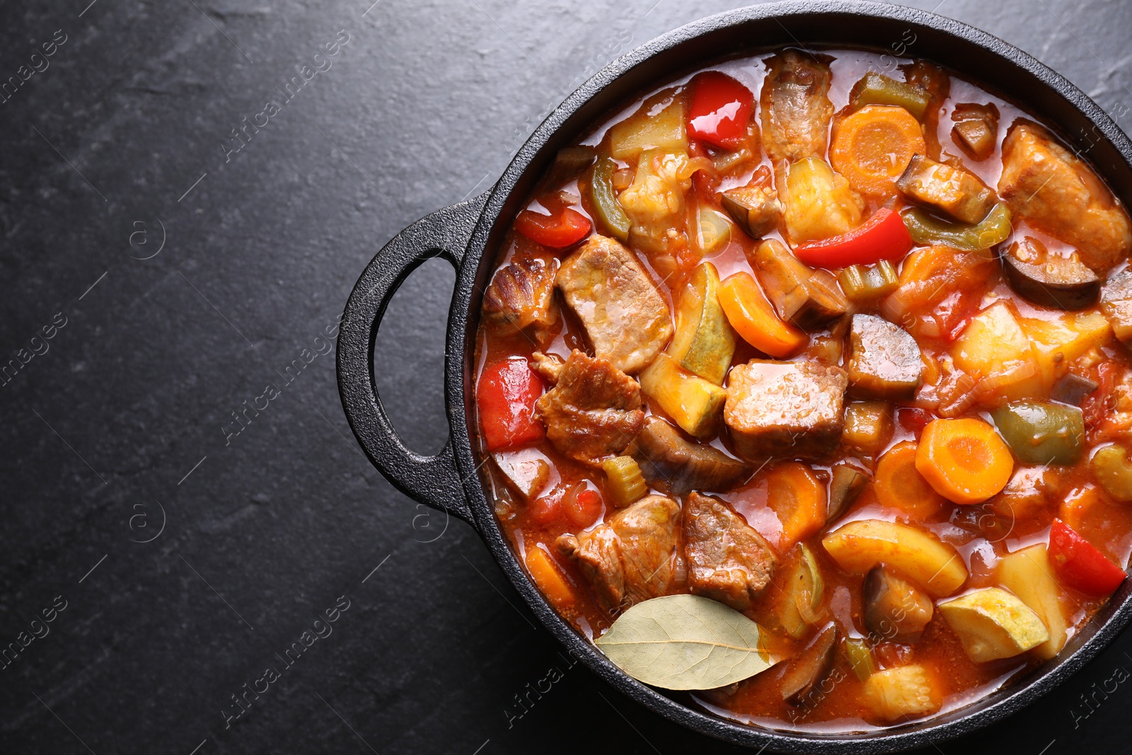 Photo of Delicious stew with vegetables in pot on gray textured table, top view. Space for text