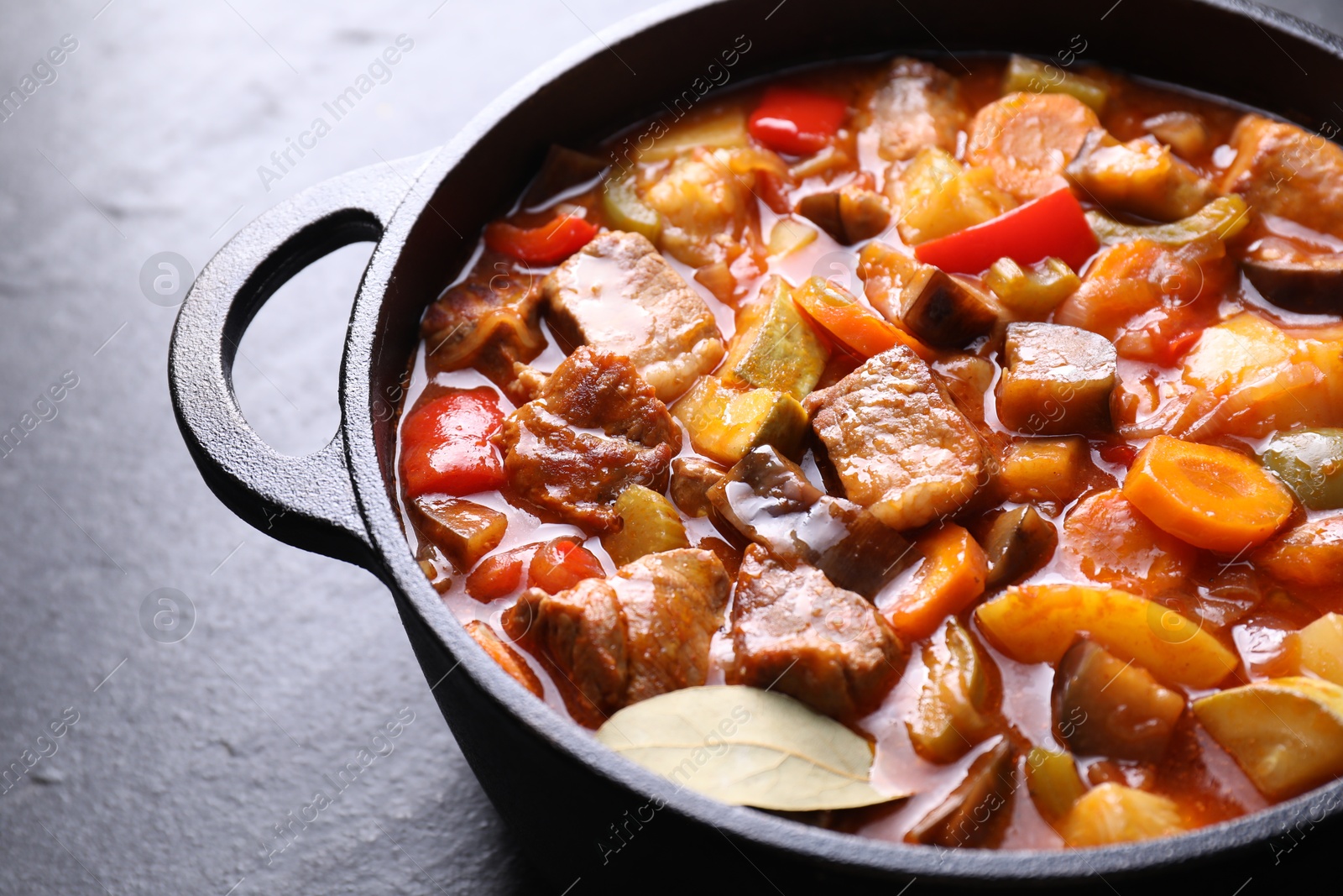 Photo of Delicious stew with vegetables in pot on gray textured table, closeup