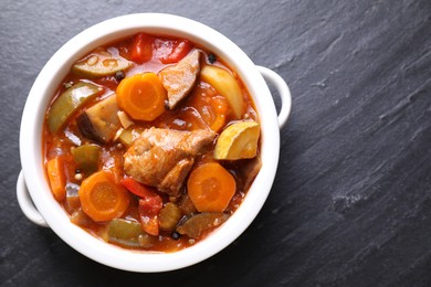 Photo of Delicious stew with vegetables in bowl on gray textured table, top view. Space for text