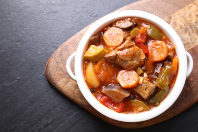 Delicious stew with vegetables in bowl on gray textured table, top view. Space for text