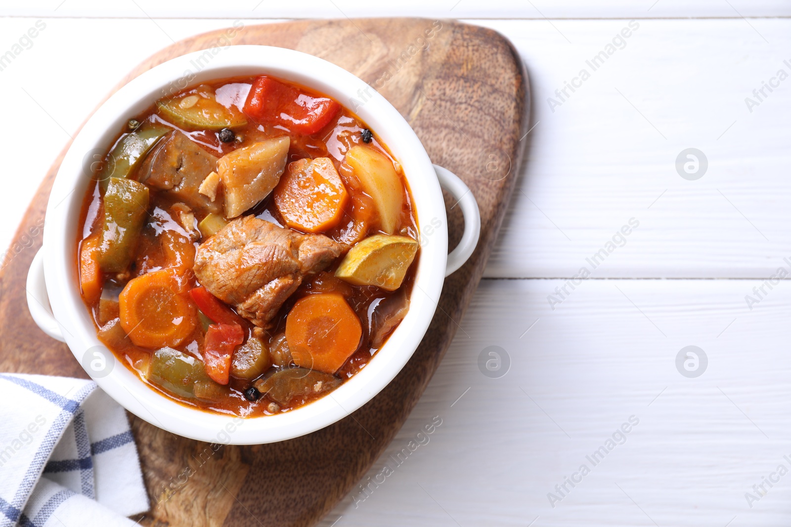 Photo of Delicious stew with vegetables in bowl on white wooden table, top view