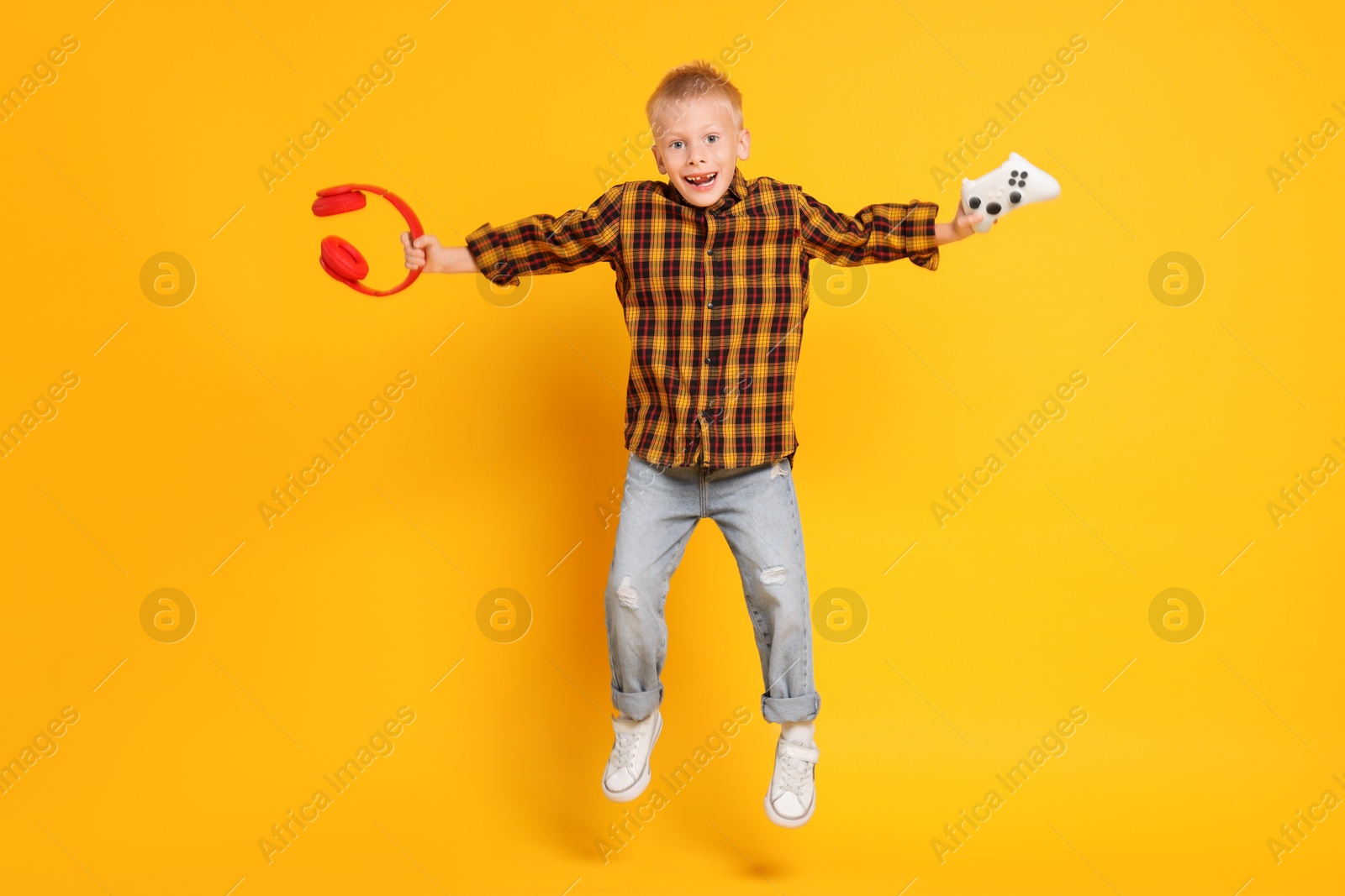 Photo of Happy little boy with controller and headphones jumping on orange background