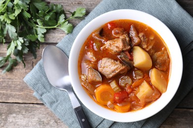 Photo of Delicious stew with vegetables in bowl, parsley and spoon on wooden table, top view