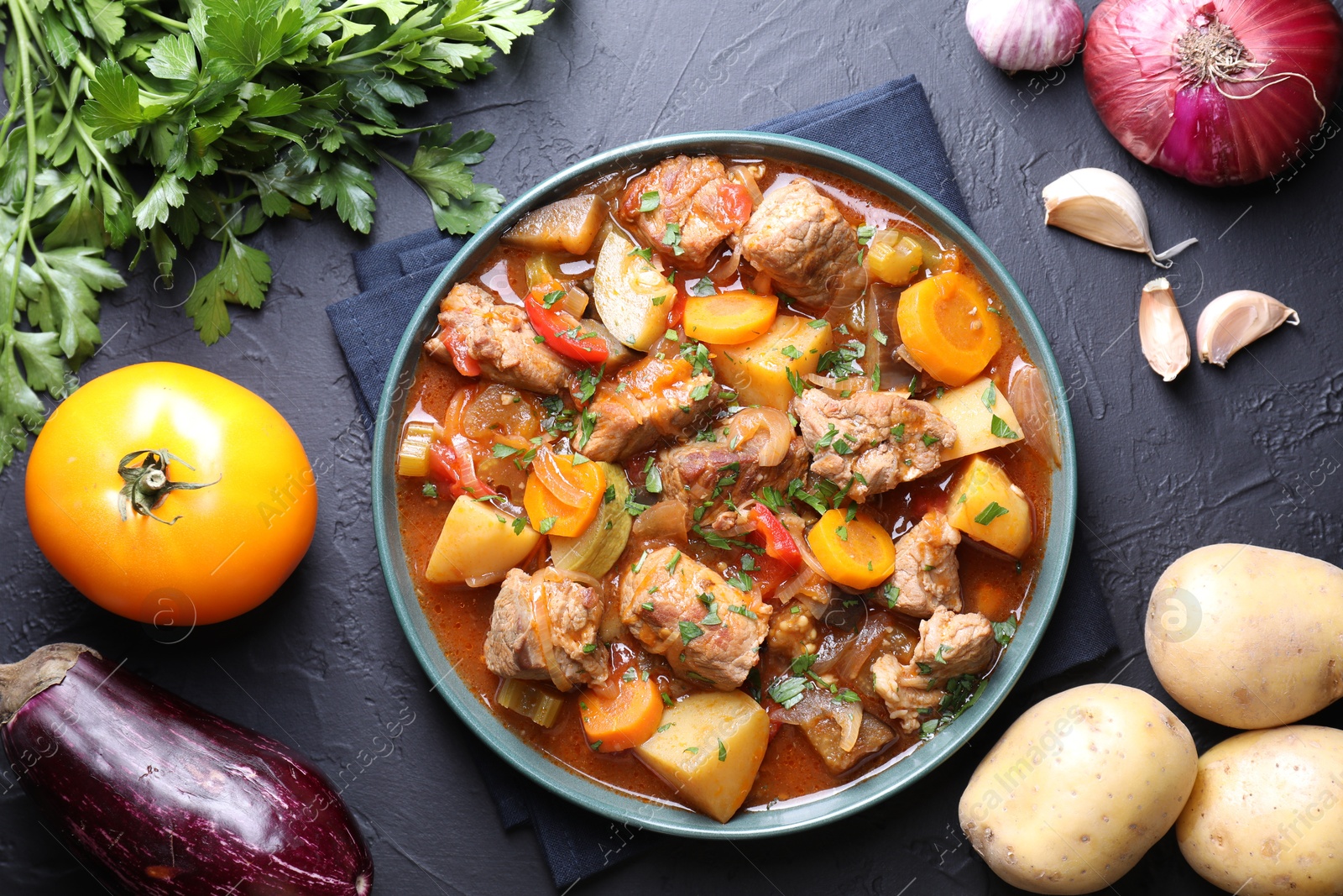 Photo of Delicious stew and different ingredients on black table, flat lay