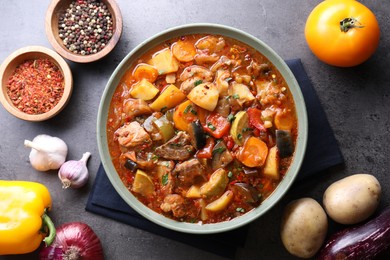 Photo of Delicious stew with vegetables in bowl and ingredients on grey table, flat lay