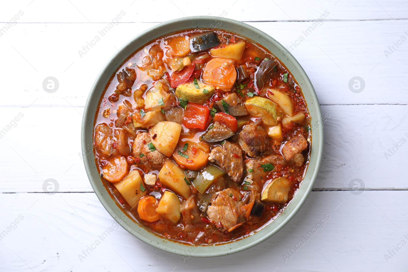 Photo of Delicious stew with vegetables in bowl on white wooden table, top view