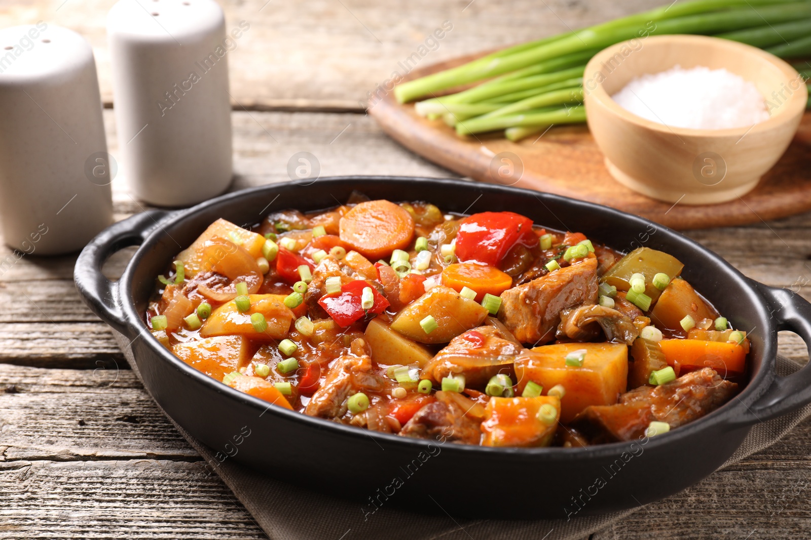 Photo of Delicious stew with vegetables in baking dish and spices on wooden table, closeup