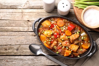 Photo of Delicious stew with vegetables in baking dish, spoon and spices on wooden table, top view