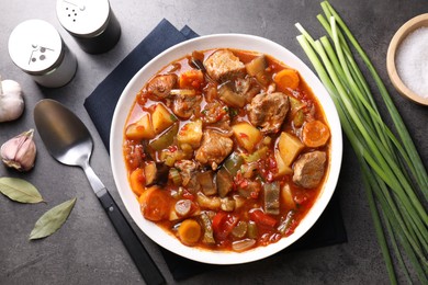 Photo of Delicious stew with vegetables in bowl, spoon and spices on grey table, flat lay